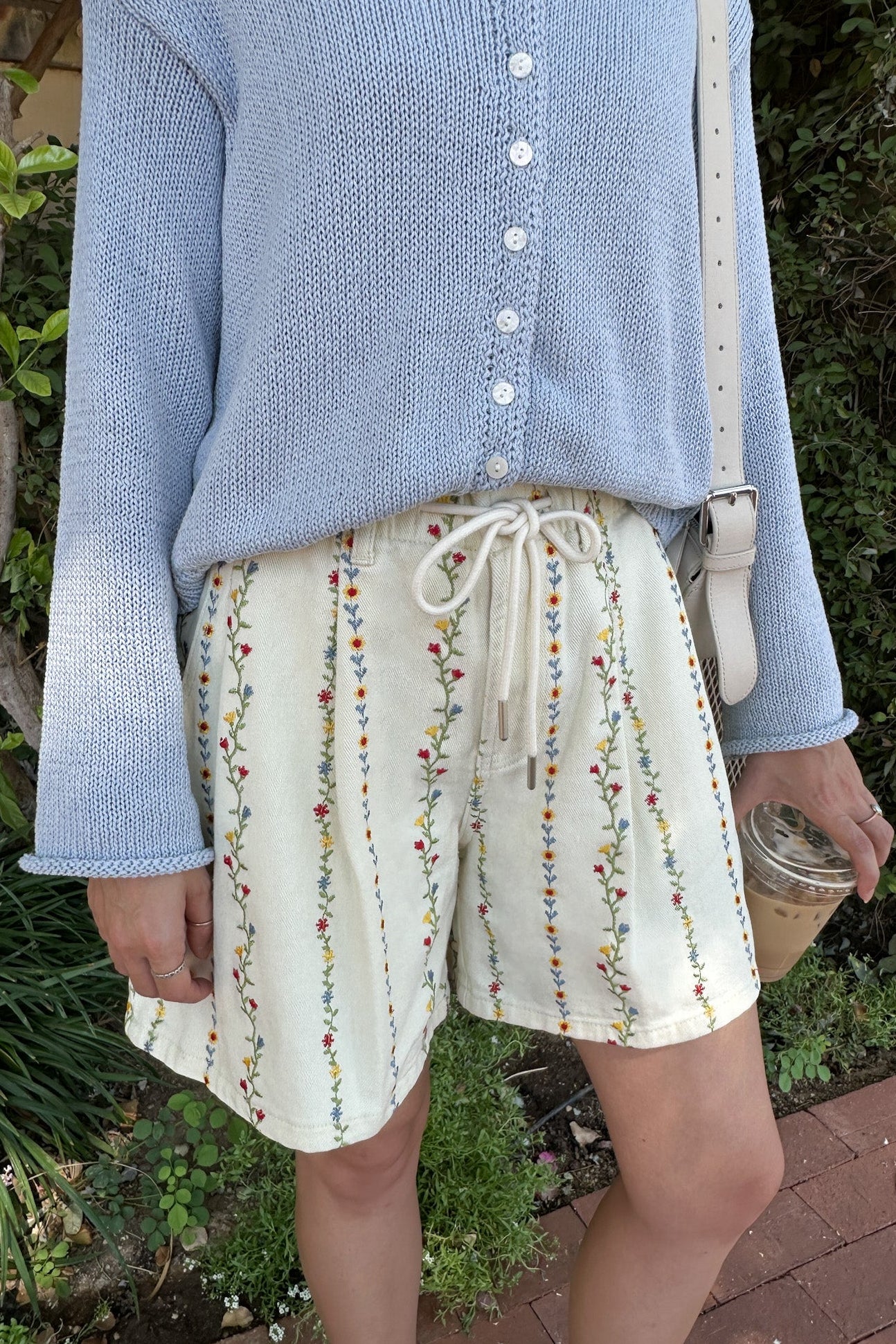Person wearing a blue sweater and floral shorts standing outdoors.