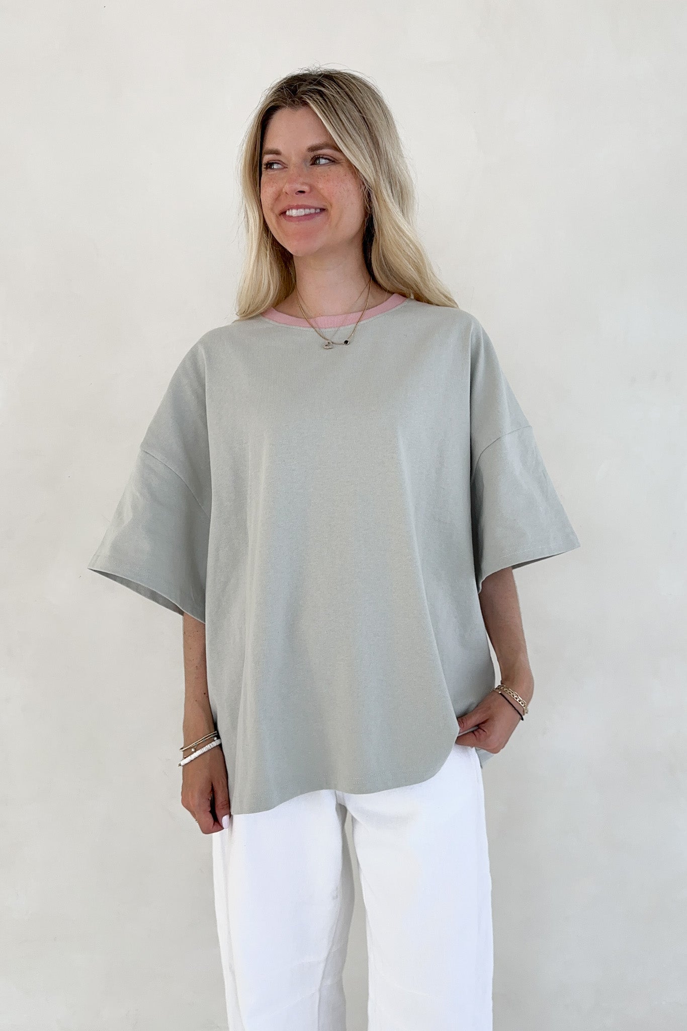 Woman wearing a light sage oversized top and white pants against a plain background