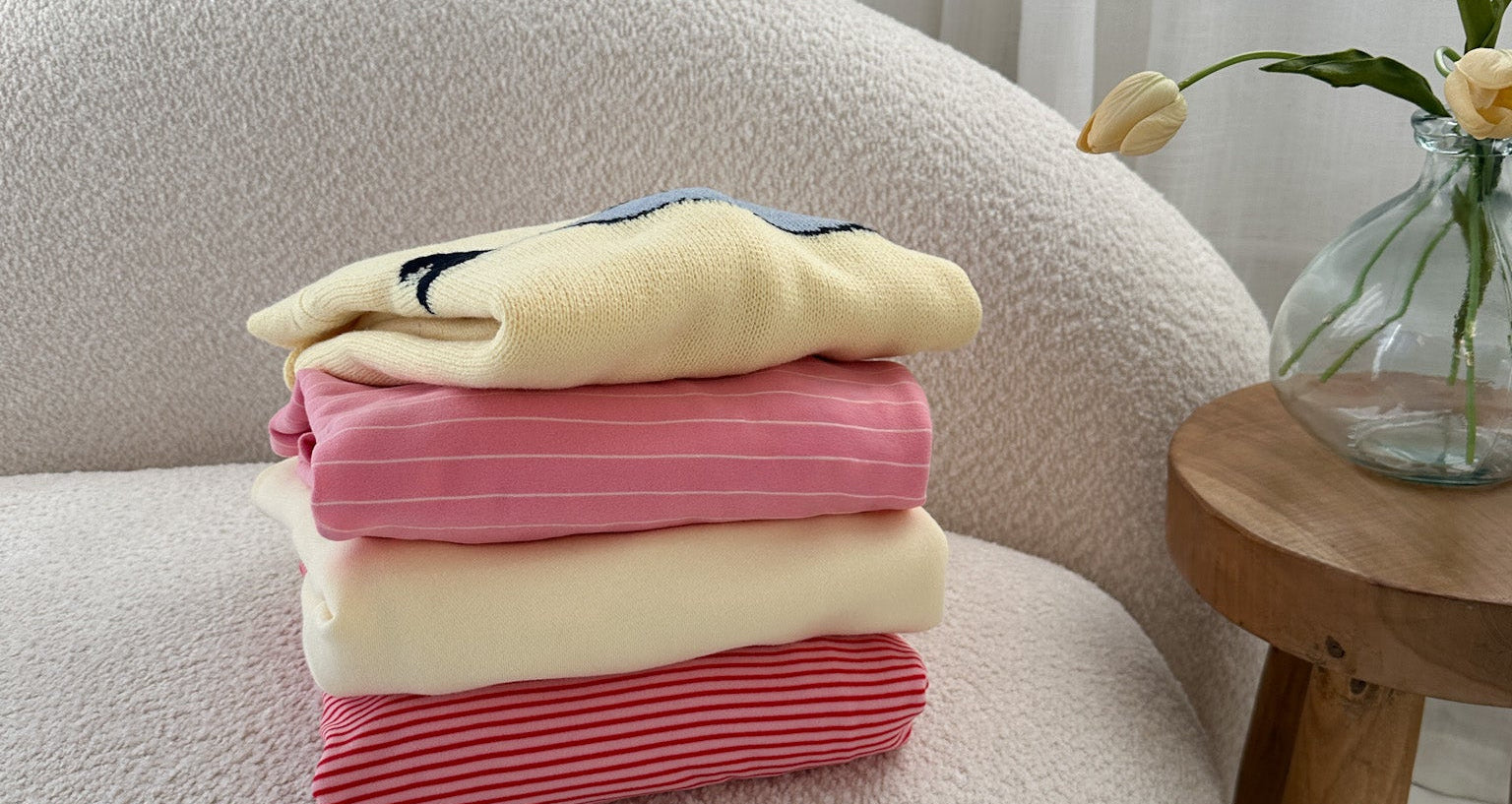 Stack of folded clothes on a chair with a vase of flowers in the background