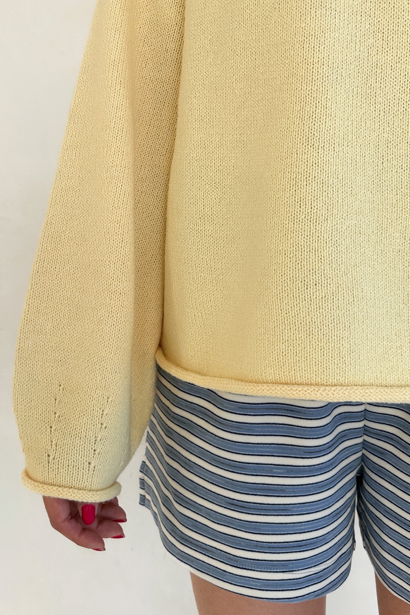 Person wearing a yellow sweater and blue and white striped shorts on a plain background
