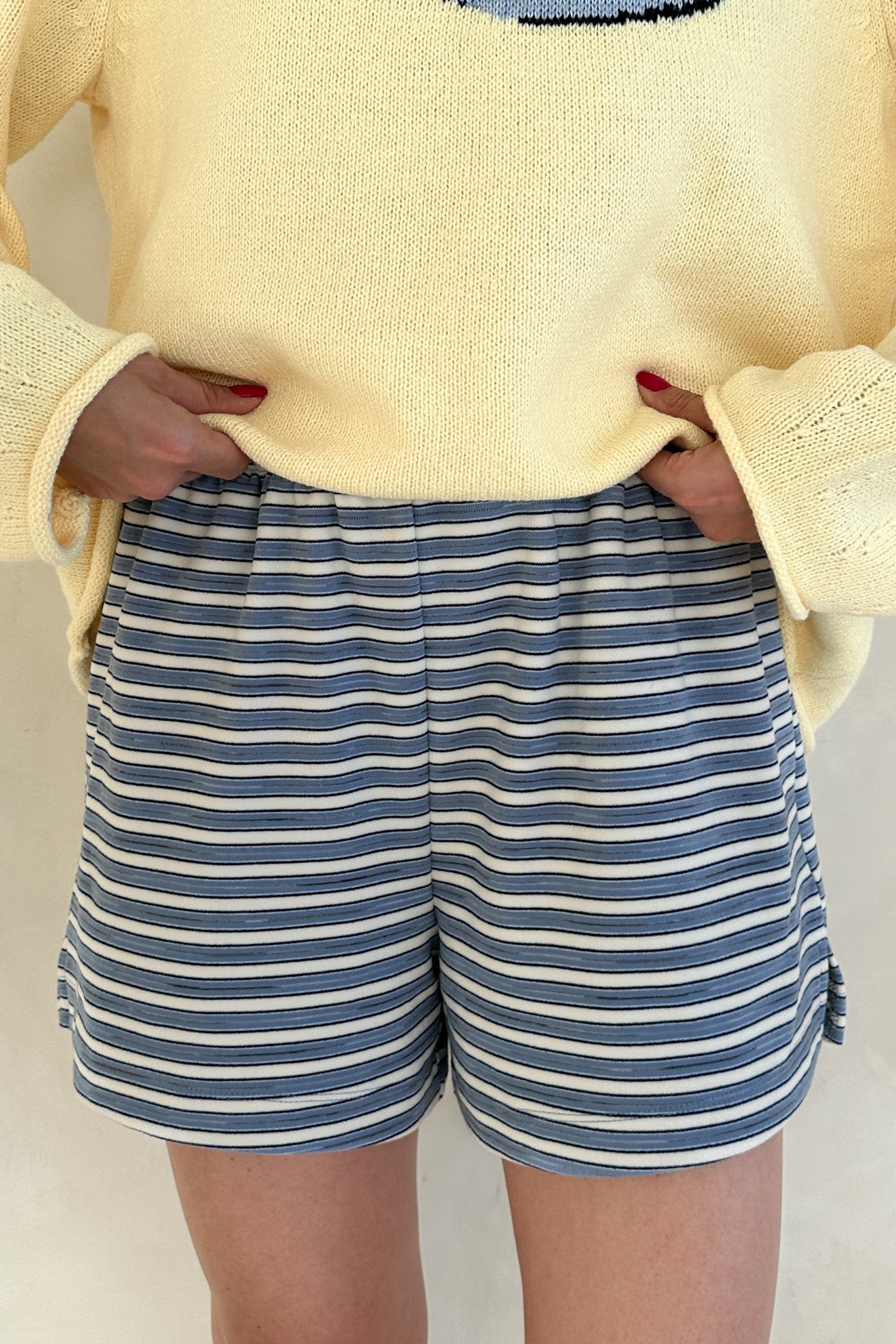 Person wearing a yellow sweater and blue and white striped shorts on a plain background