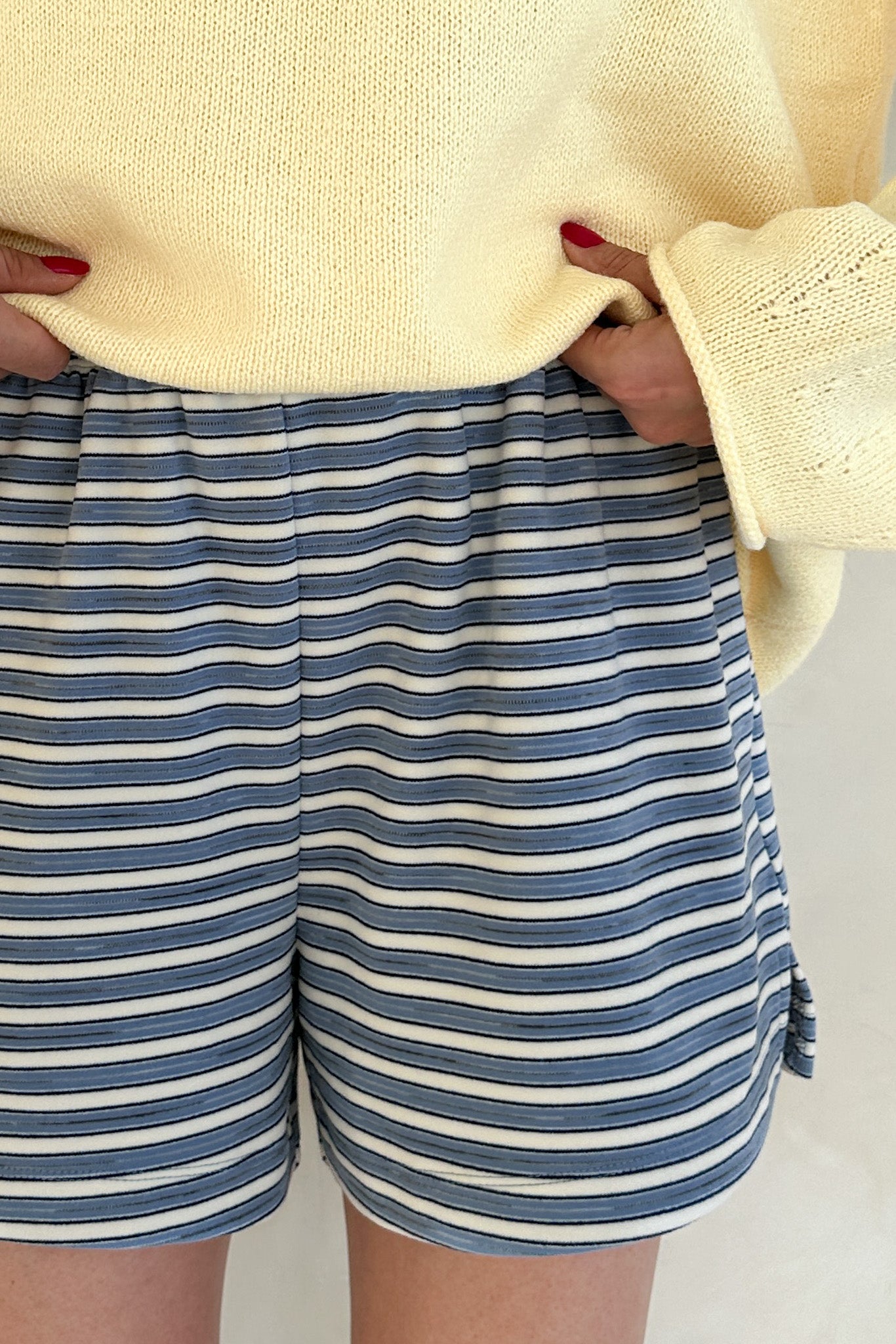 Person wearing blue and white striped shorts with a light yellow sweater.