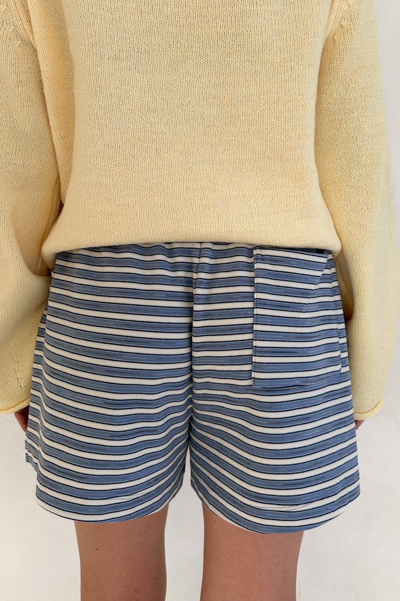 Person wearing blue and white striped shorts with a beige sweater on a plain background