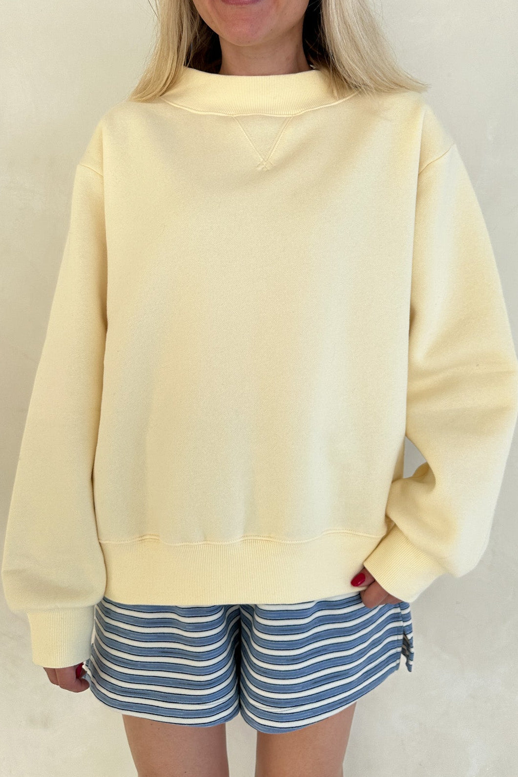 Woman wearing a light yellow sweatshirt and striped shorts against a plain background