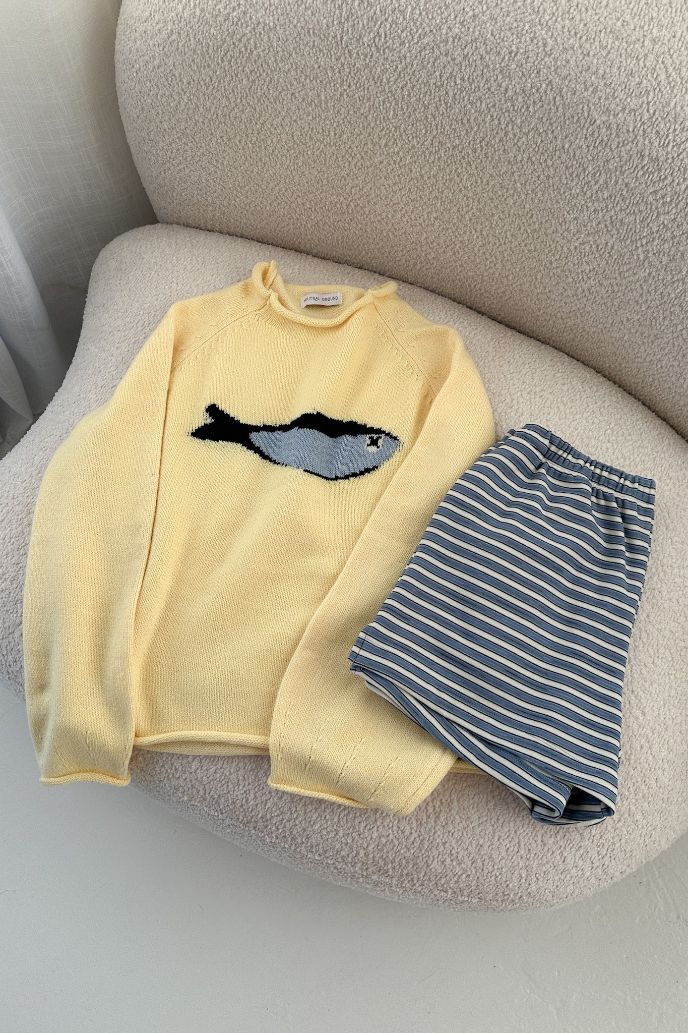 Yellow sweater with fish design and striped pants on a beige chair