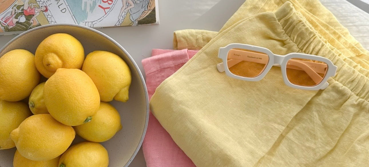 Lemons in a bowl with yellow pants and sunglasses on a table