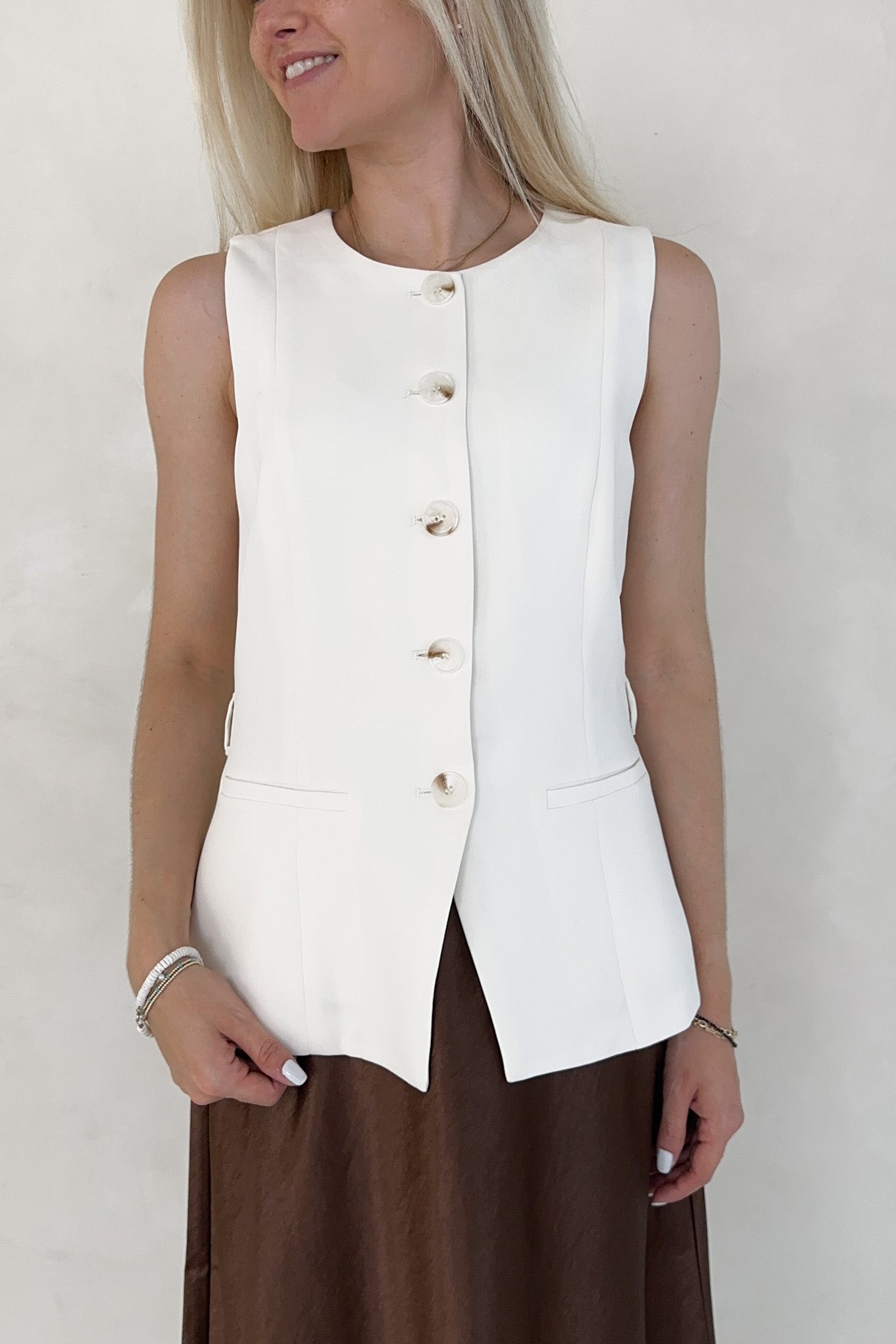 Woman wearing a white sleeveless blazer against a plain background