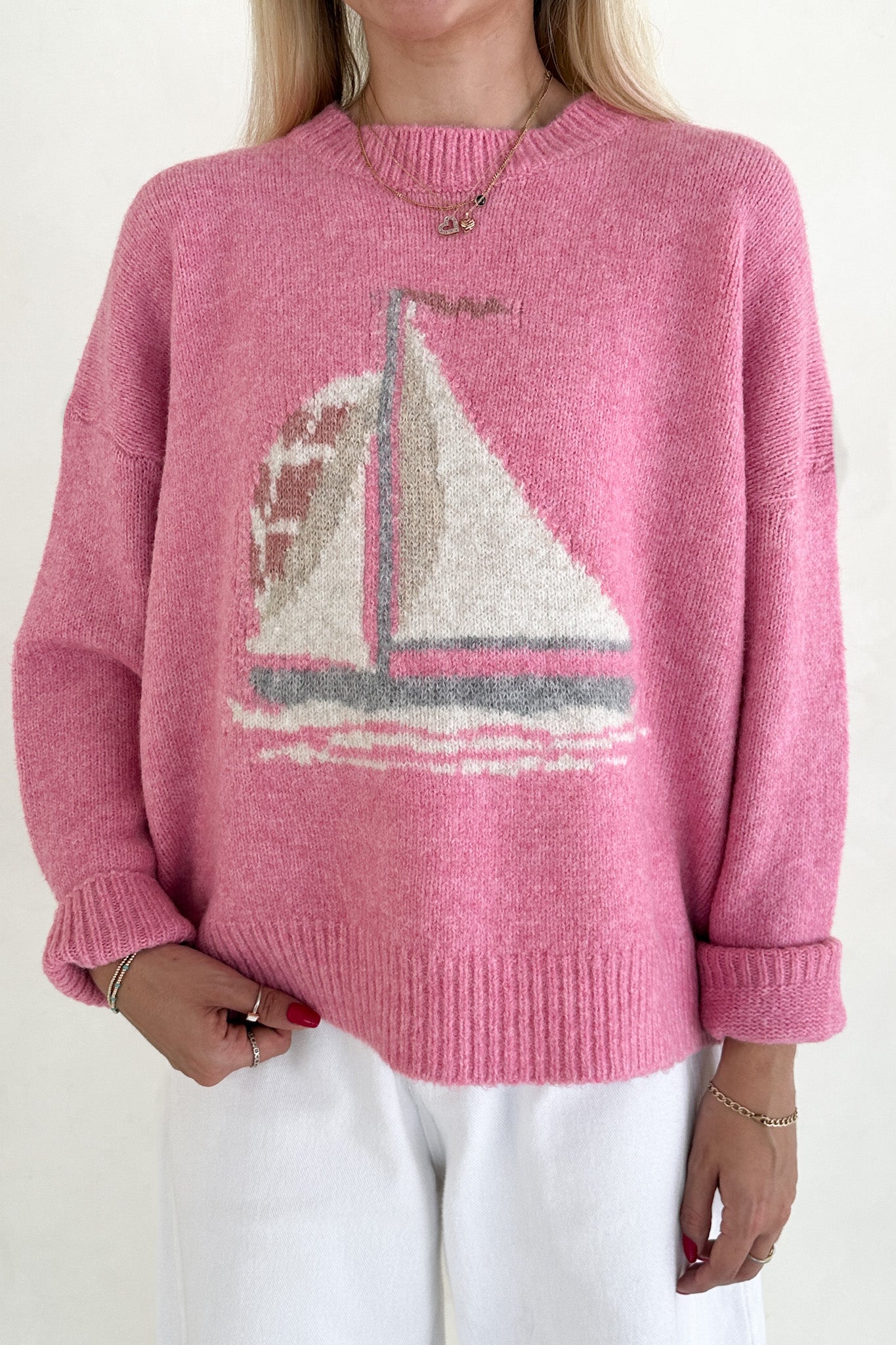 Person wearing a pink sweater with a sailboat design on a white background