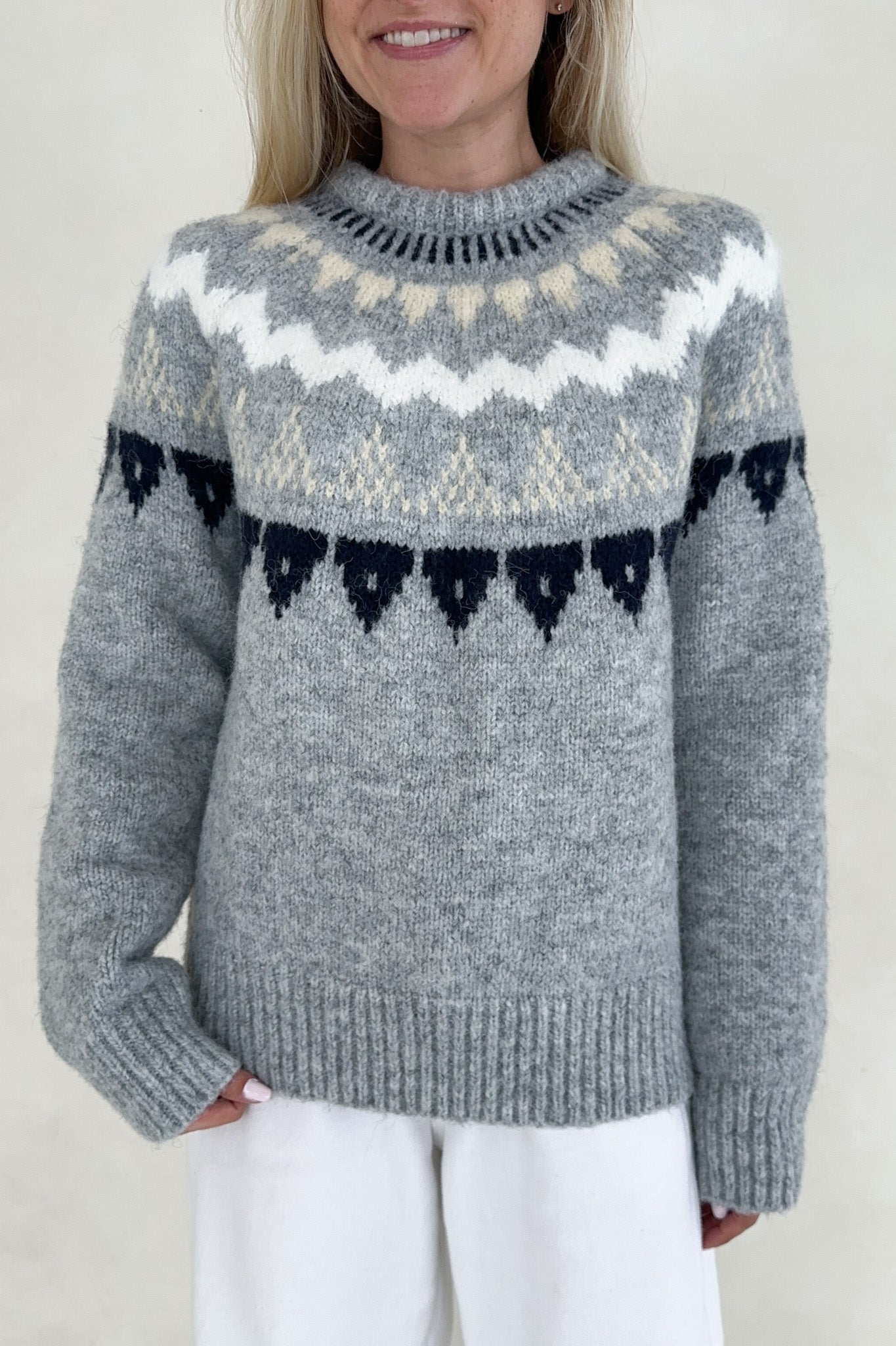 Person wearing a gray knitted sweater with a pattern, standing against a plain background