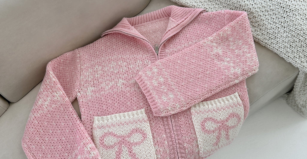Pink knitted baby sweater with white patterns on a beige surface