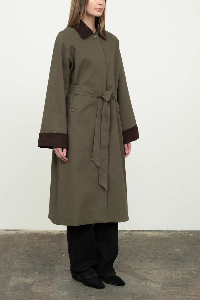 Woman wearing a long olive green coat with a belt against a white background